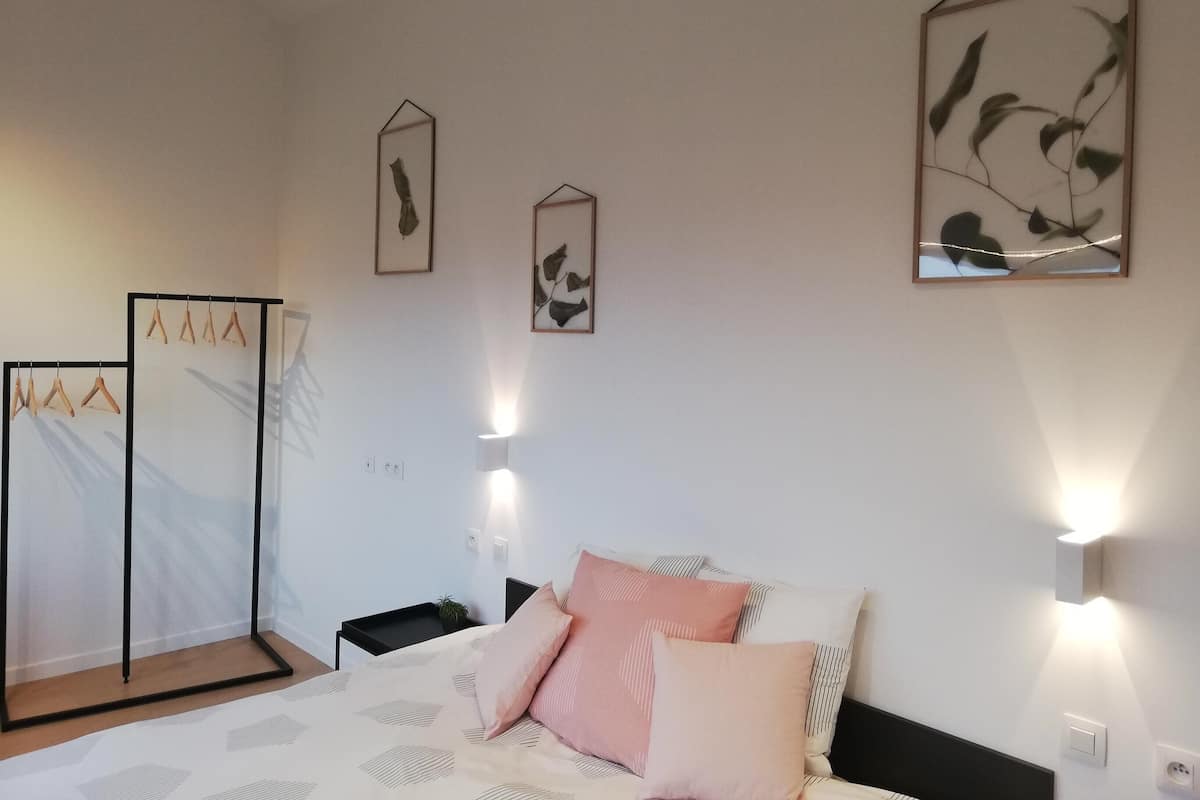 Quarto com cama, mesas de cabeceira, luminárias fixadas na parede e quadros.