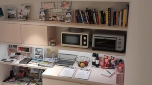 Een kleine kitchenette met een magnetron, een broodrooster, een spoelbak en een aanrecht met diverse spullen zoals boeken, tijdschriften en een mand.