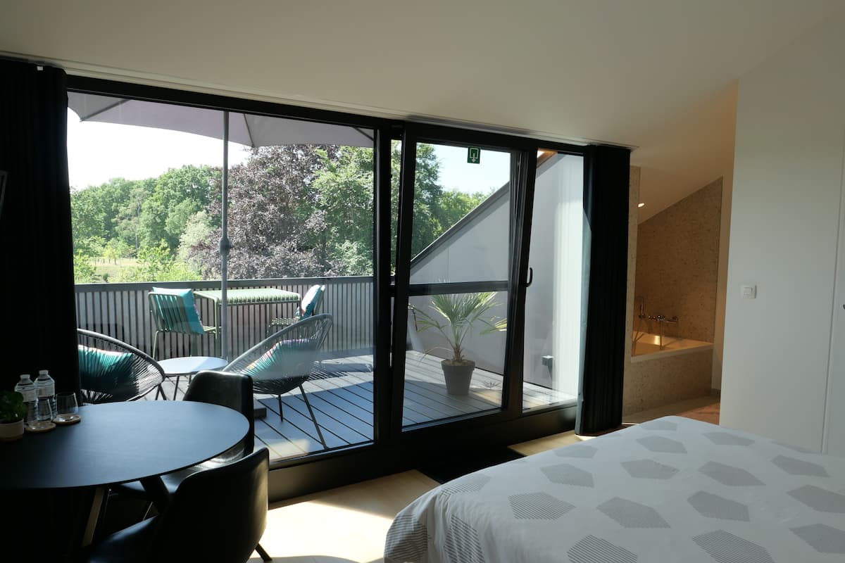 Quarto com uma grande porta de correr de vidro que dá para uma varanda com mobiliário e vista para árvores.
