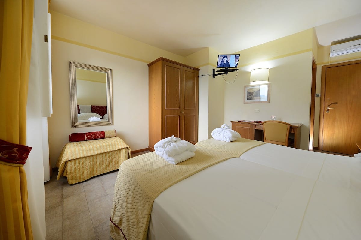 Ein Hotelzimmer mit zwei Betten, einem Holzschrank, einem Spiegel, einem Fernseher und einem Schreibtisch mit Lampe.