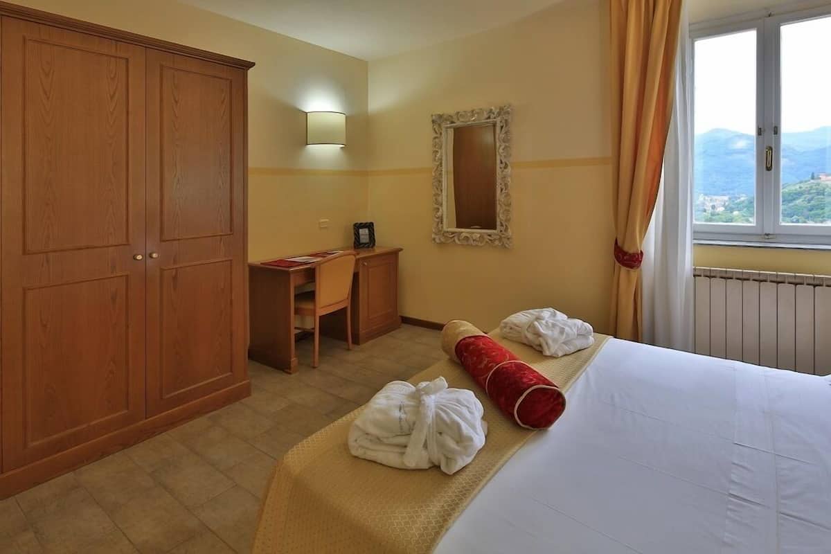 Ein Hotelzimmer mit Bett, Schreibtisch, Kleiderschrank, Spiegel und Fenster mit Aussicht.