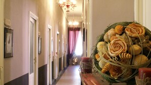 A hallway with a chandelier, framed pictures on the walls, and a decorative floral arrangement on a table. - Hotel & terme Bagni di Lucca (Bagni di Lucca)
