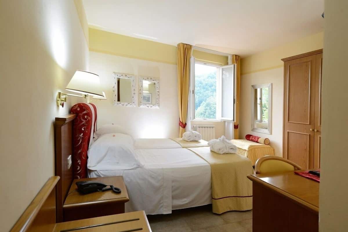 Ein Hotelzimmer mit zwei Betten, einem Schreibtisch, einem Stuhl, einer Lampe und einem Fenster mit Vorhängen.
