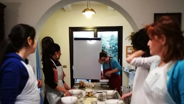 Un grupo de personas en una habitación con una larga mesa dispuesta para una comida, una pizarra y una puerta que da al exterior.