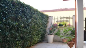 Un patio con piso de baldosas, un seto y varias macetas con plantas.
