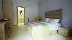 Un dormitorio con cama, mesita de noche y escritorio con silla. Se ve un baño a través de una puerta abierta.