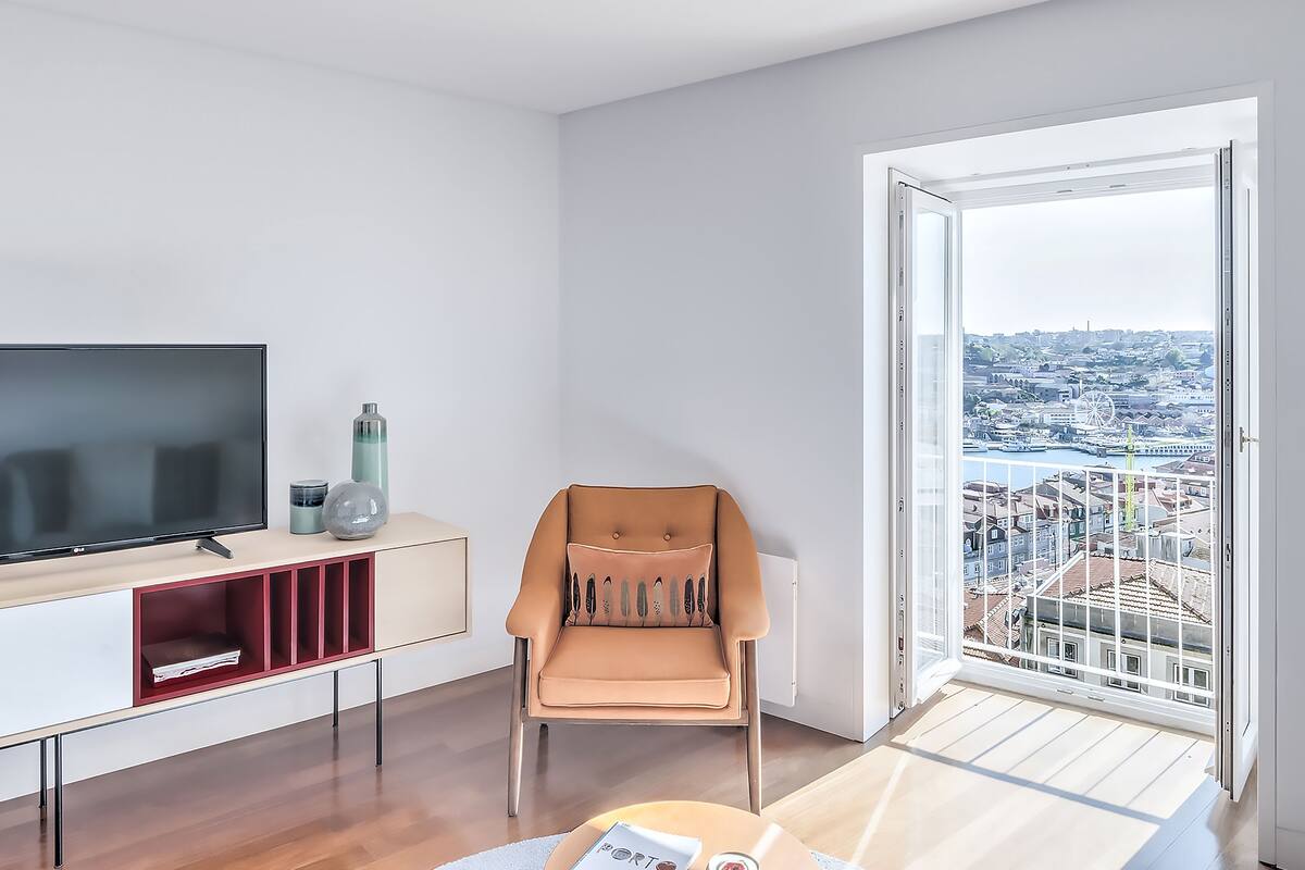 A modern living room with a large TV, a comfortable chair, and a view of a cityscape through a large window.
