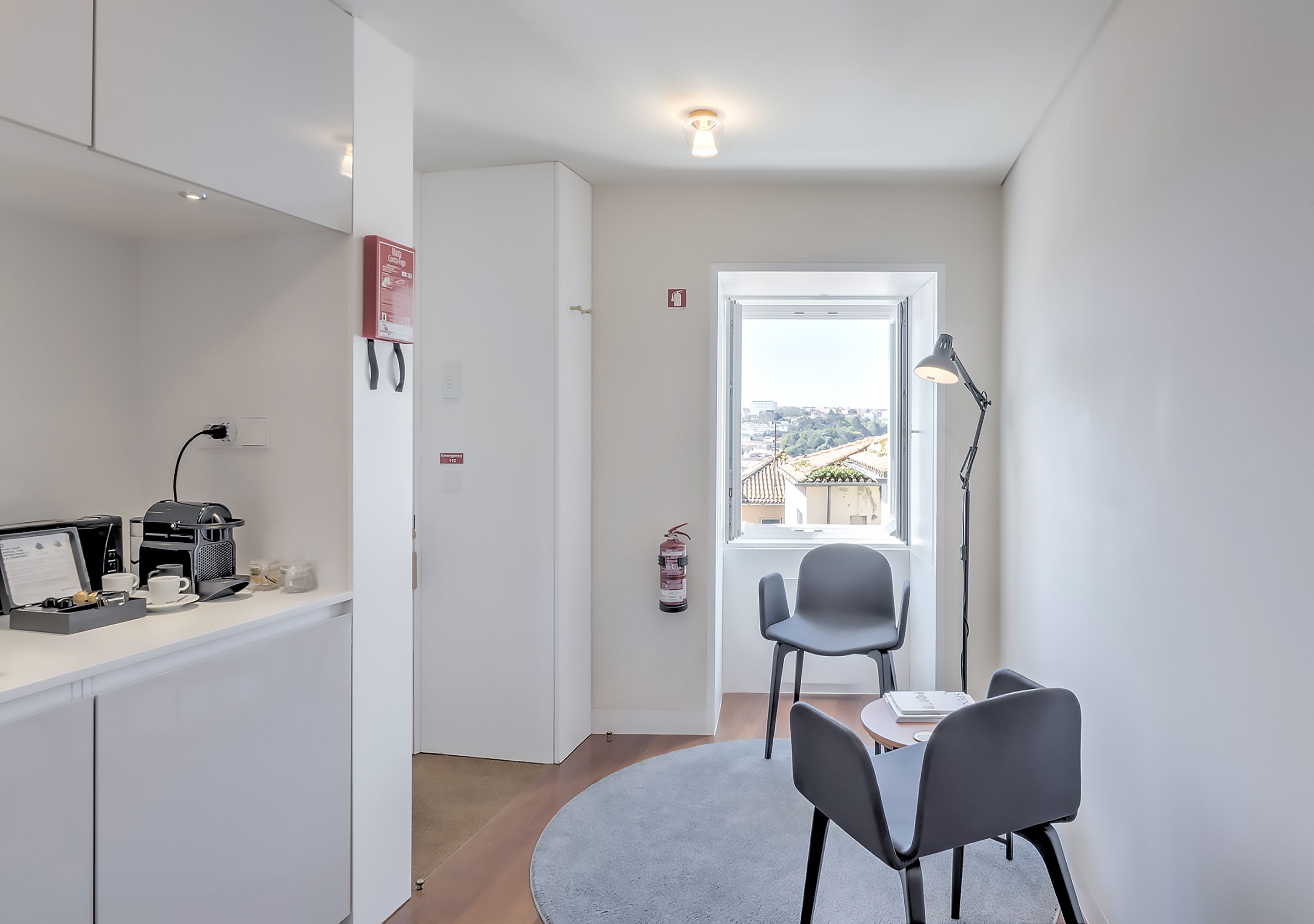 Une petite cuisine équipée avec une machine à café, une petite table et deux chaises. Un extincteur est fixé au mur, près de la porte.