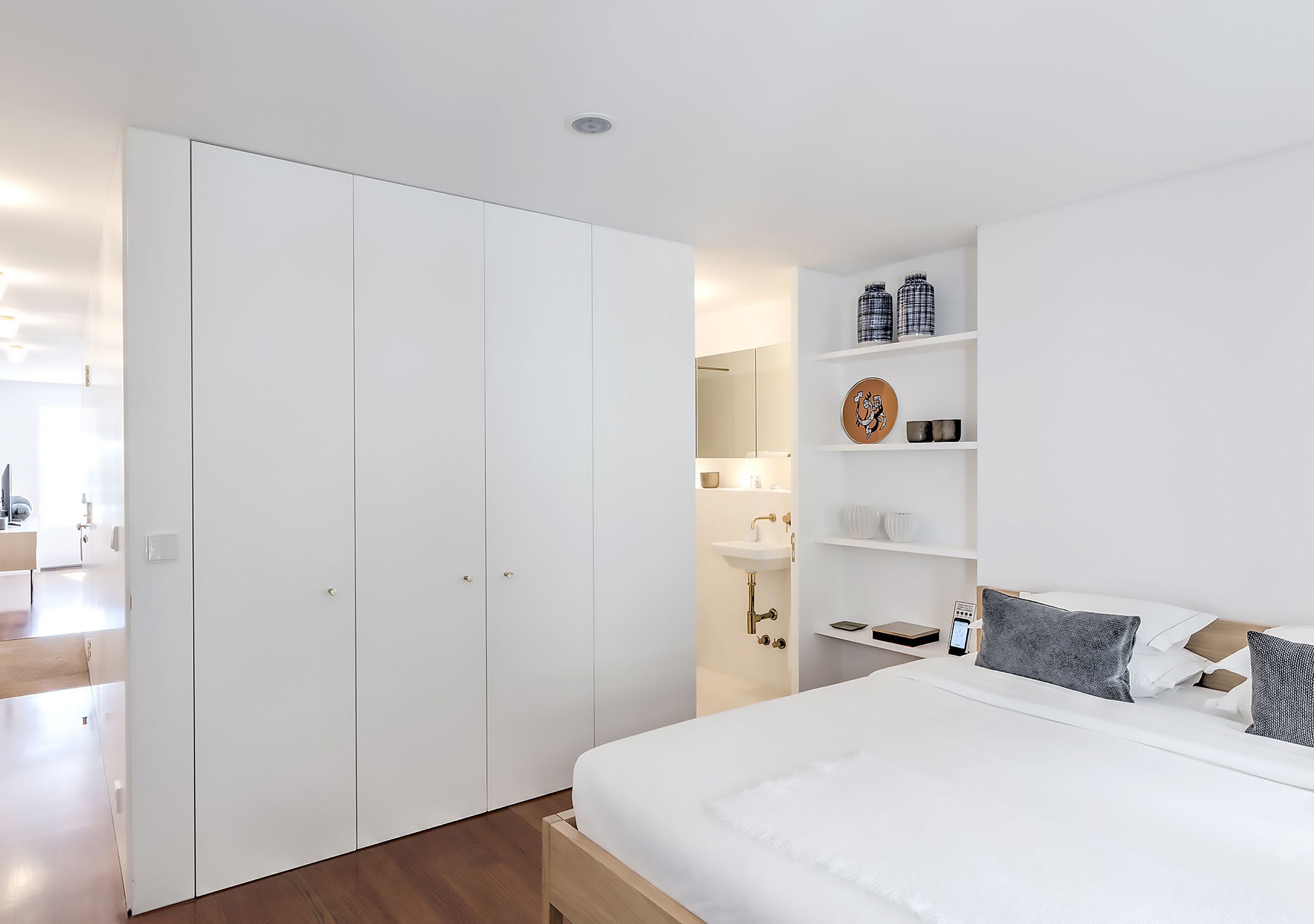 Ein modernes Schlafzimmer mit einem großen Bett, einem weißen Kleiderschrank und Einbauschränken mit Dekorationselementen.