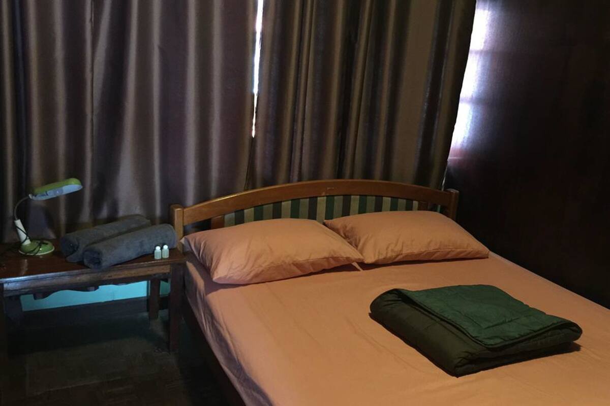 A hotel room with a bed, pillows, a bedside table with a lamp, and a window with curtains.