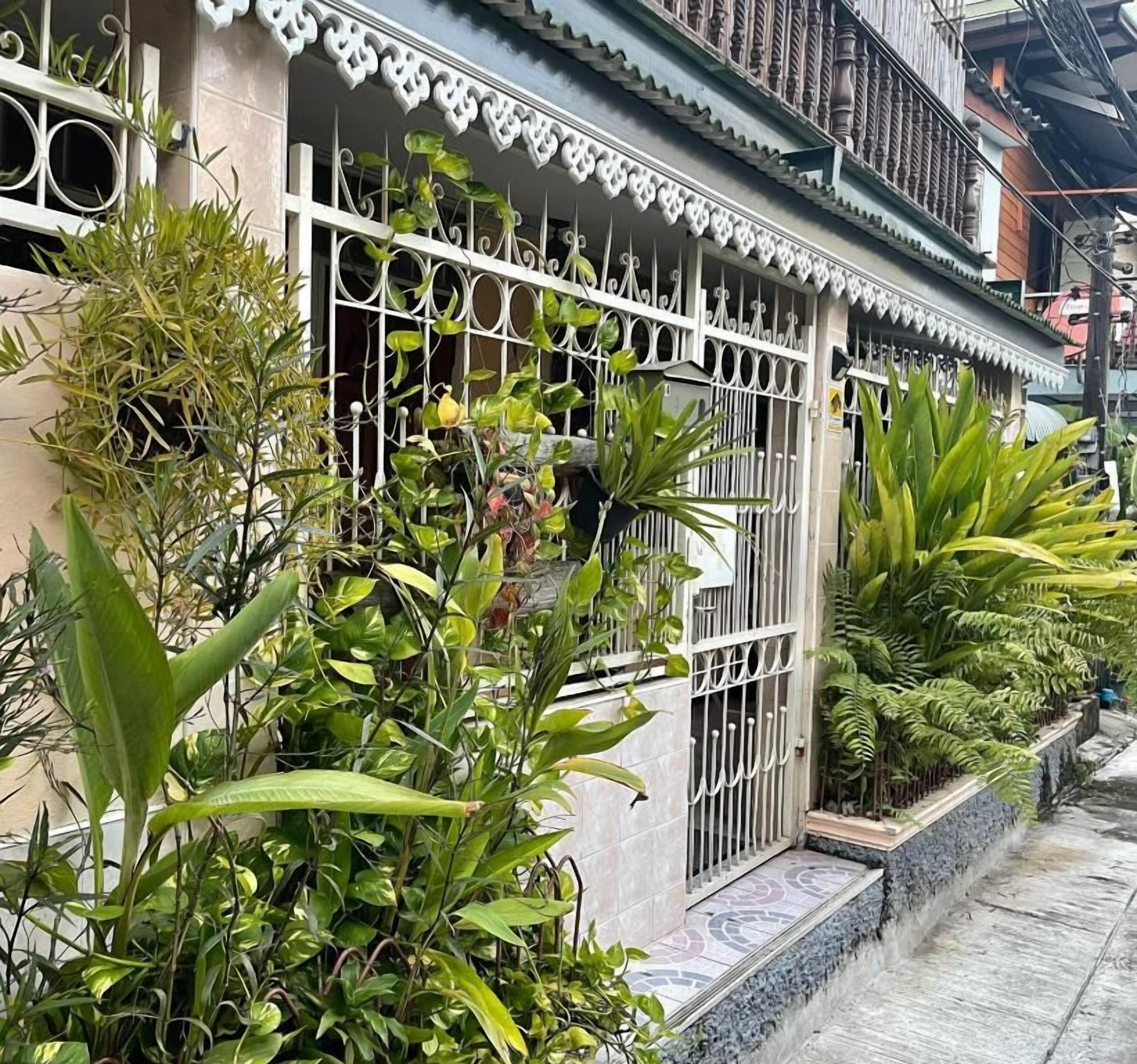 A building with a gated entrance, surrounded by lush greenery and a tiled pathway.
