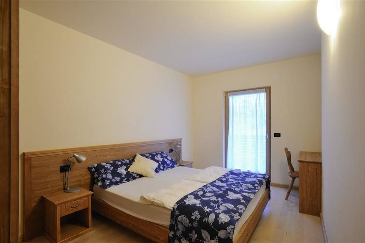 A bedroom with a wooden bed, a nightstand, a desk, and a chair.