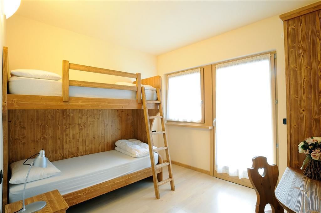 Una camera con un letto a castello, una scala in legno, una scrivania con una lampada e una finestra con tende.