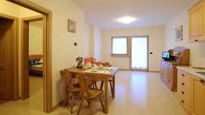 Quarto com uma mesa de jantar de madeira, cadeiras, pequena cozinha com armários de madeira e uma janela que proporciona iluminação natural.