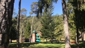 Um parque com parquinho infantil, incluindo um escorregador e estrutura de escalada, cercado por árvores altas e uma área para piquenique.