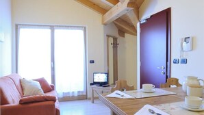Quarto com teto de madeira, sofá, mesa de jantar com cadeiras, televisão e uma porta.