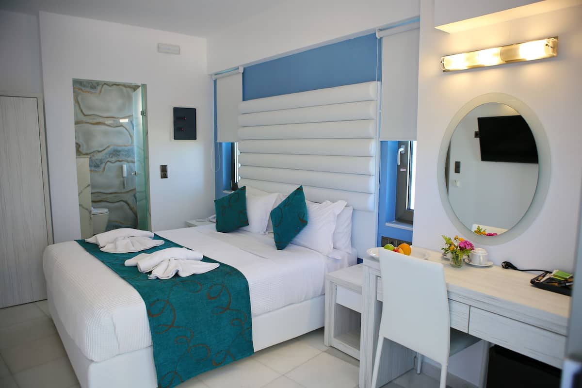 A hotel room with a bed, a desk, a chair, a mirror, and a bathroom door.