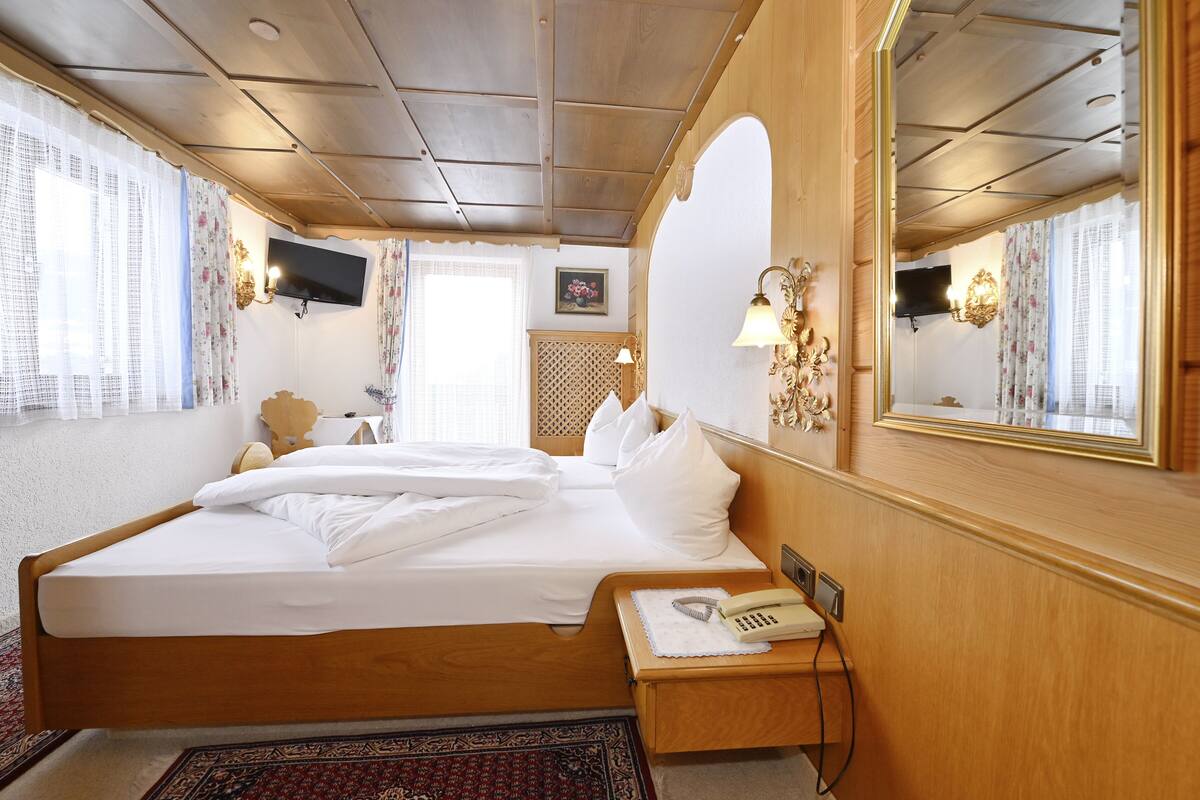 A hotel room with a large bed, a bedside telephone, a mirror, and a television mounted on the wall.