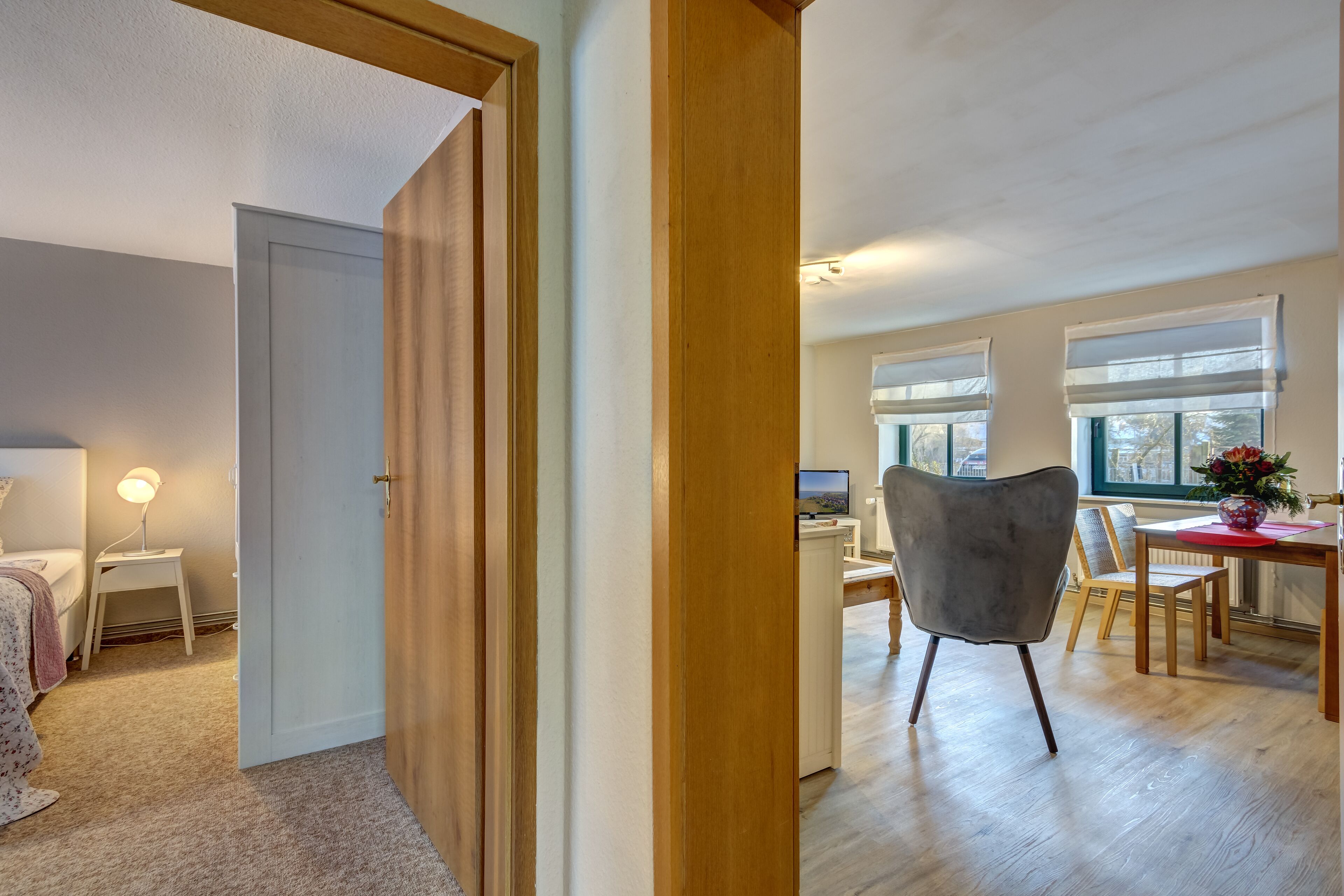 Un salon moderne avec un plancher en bois, un coin repas comprenant une table et des chaises, et une chambre à coucher avec un lit et une lampe.