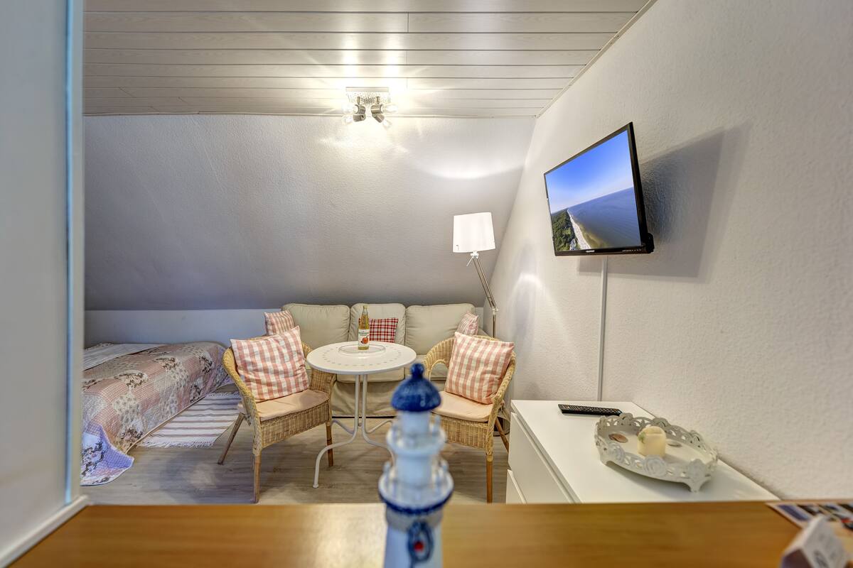 Una habitación acogedora con una cama, un sofá, una mesita redonda y un televisor montado en la pared.
