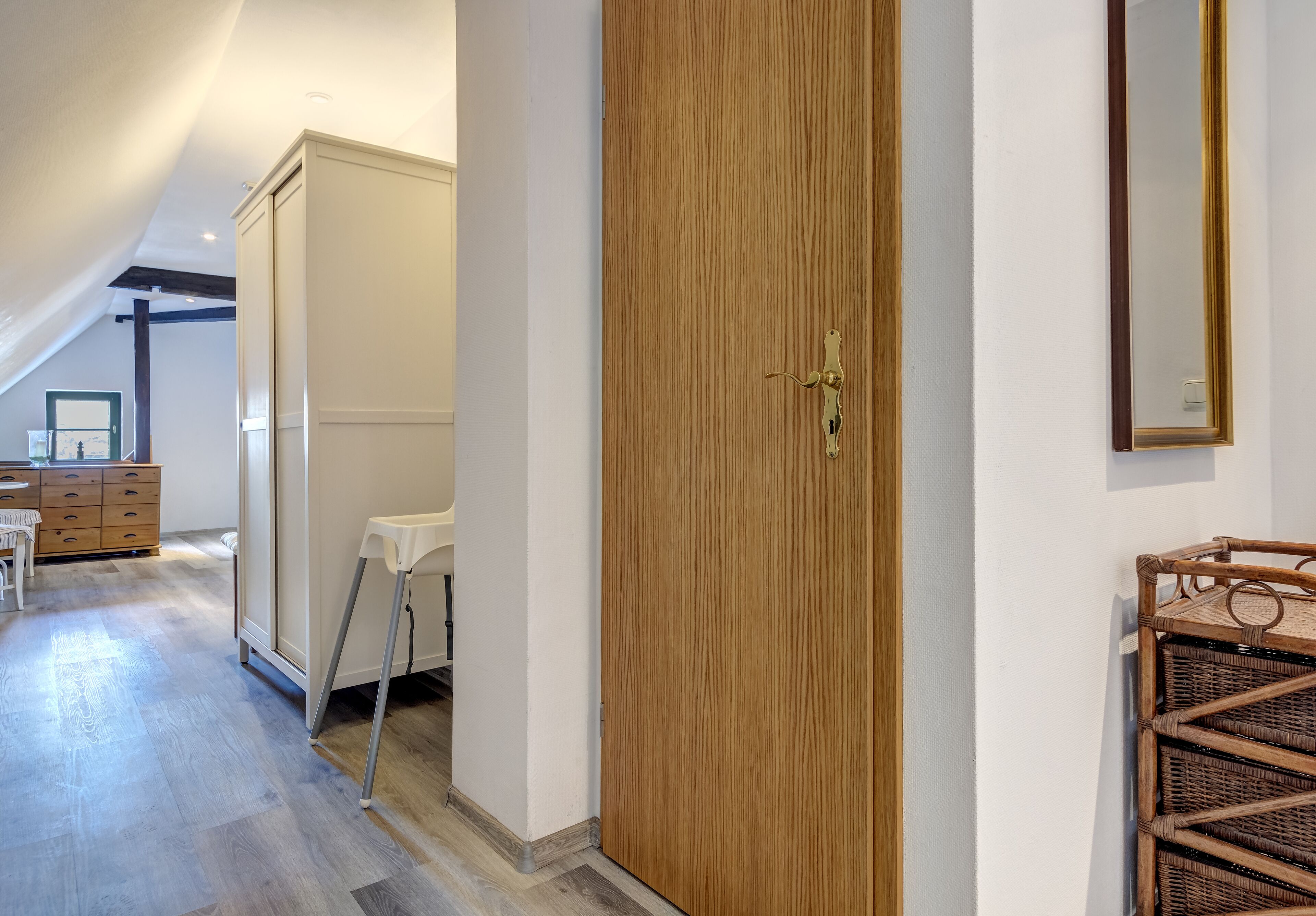 A hallway with a wooden door, a white chair, a small table, and a wicker basket.