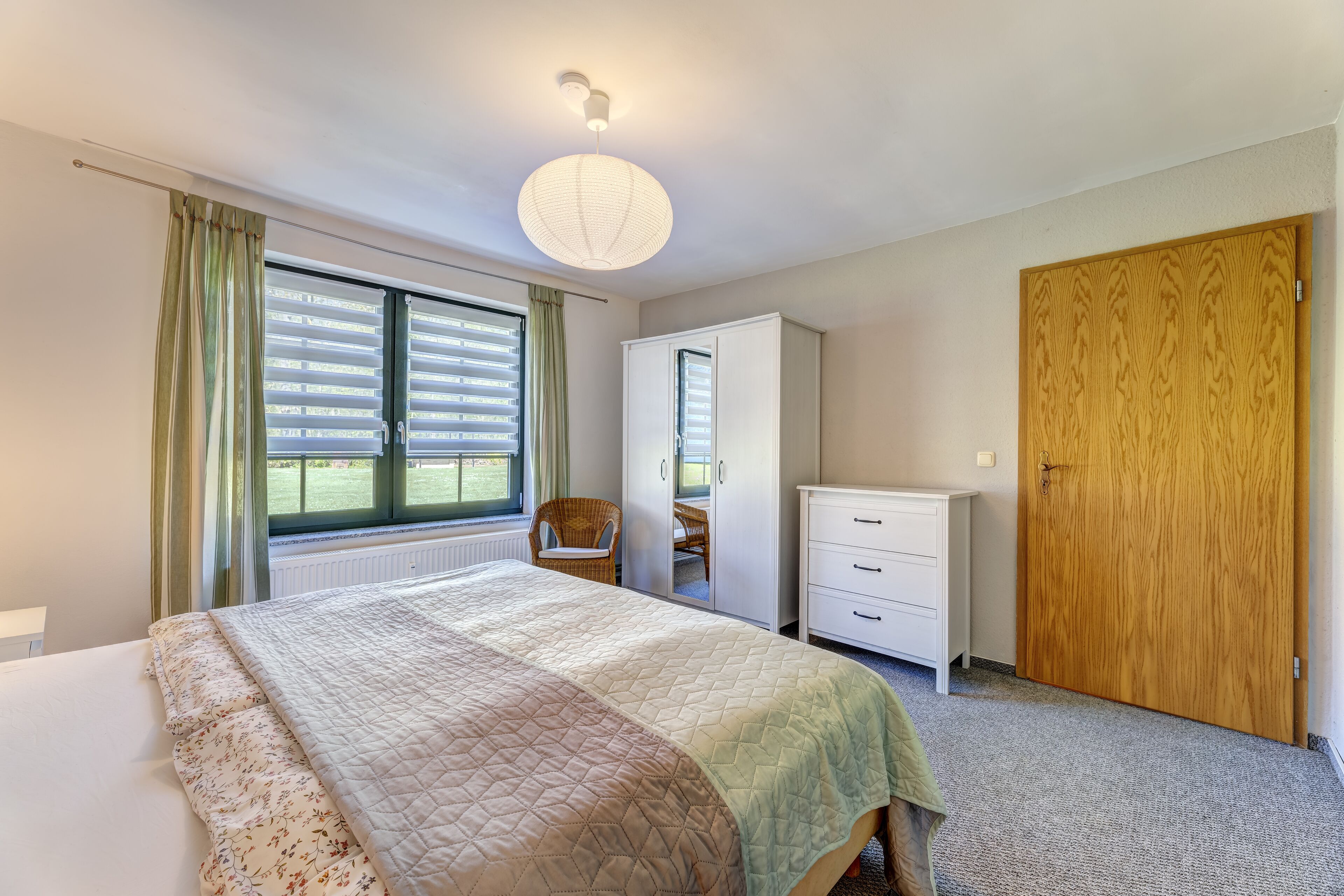 Ein Schlafzimmer mit einem Bett, einem Kleiderschrank, einem Stuhl und einem Fenster mit Vorhängen.