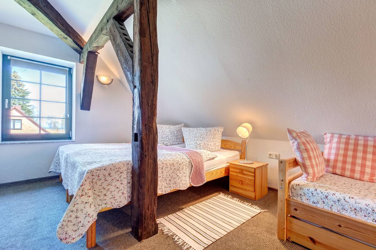 Un dormitorio acogedor con un cabecero de madera, una mesita de noche, un pequeño aparador de madera y una ventana con vistas a una casa.