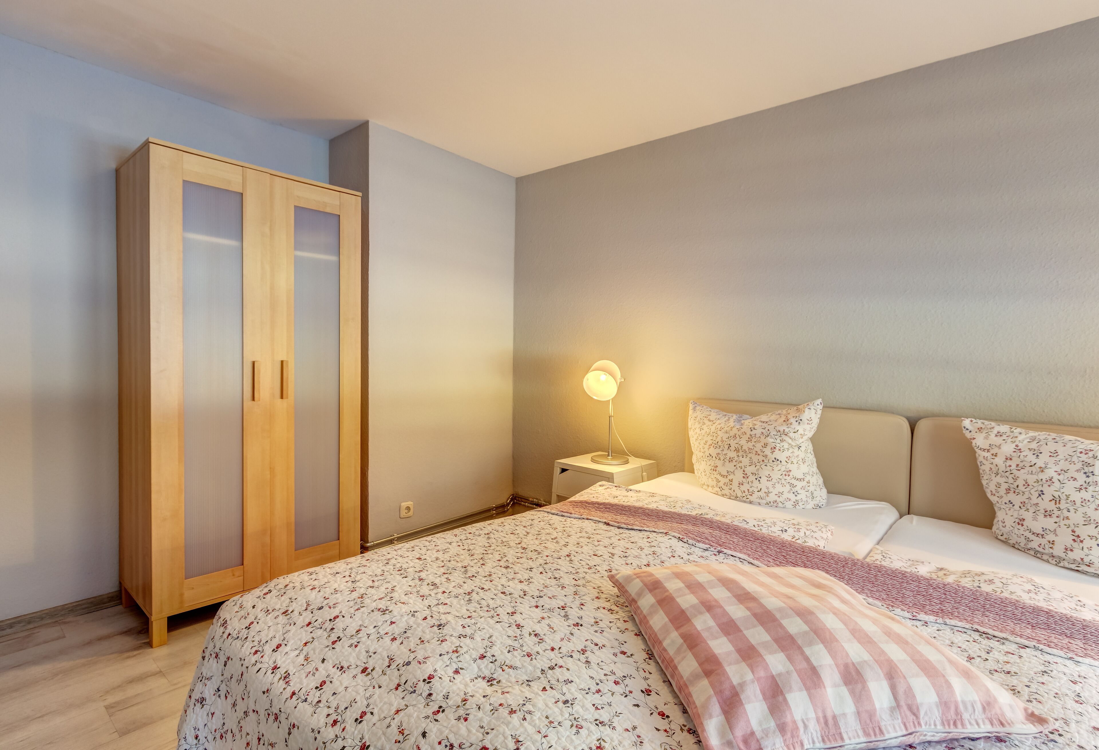 Une chambre à coucher comprenant un lit, une armoire, une table de chevet avec une lampe et une literie à motifs floraux.