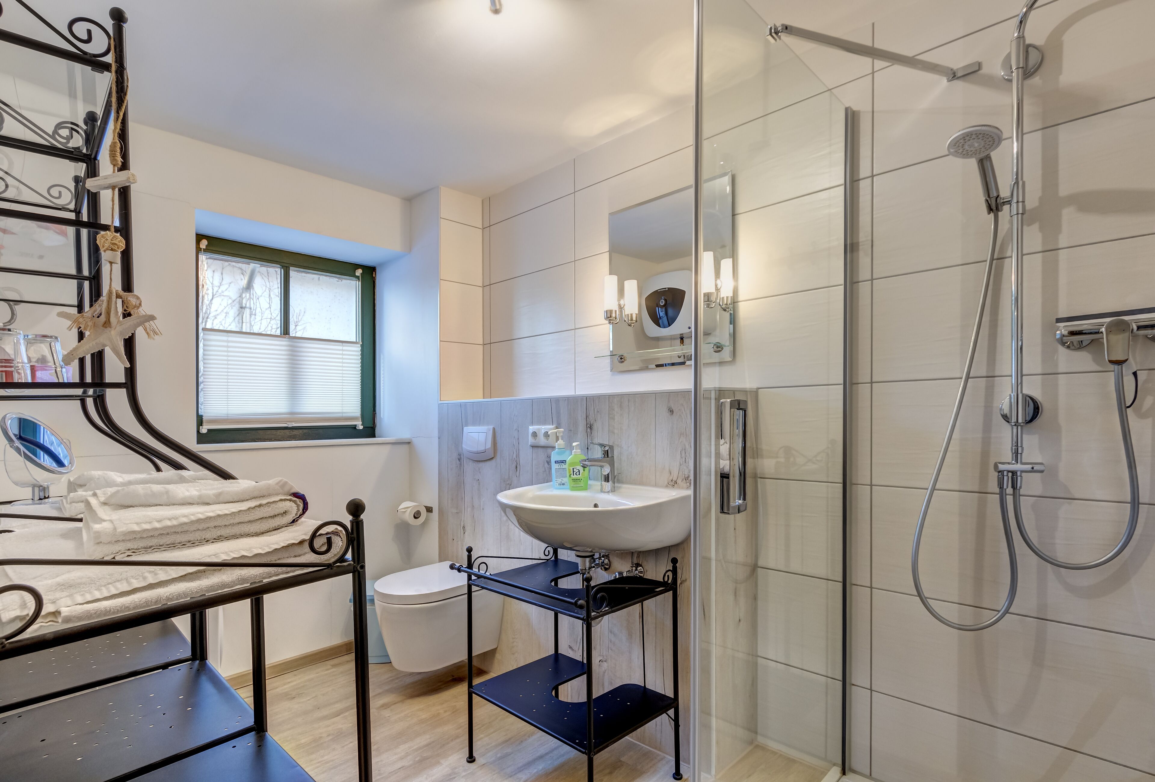 A modern bathroom with a glass shower enclosure, a white sink, and a black metal rack with towels.