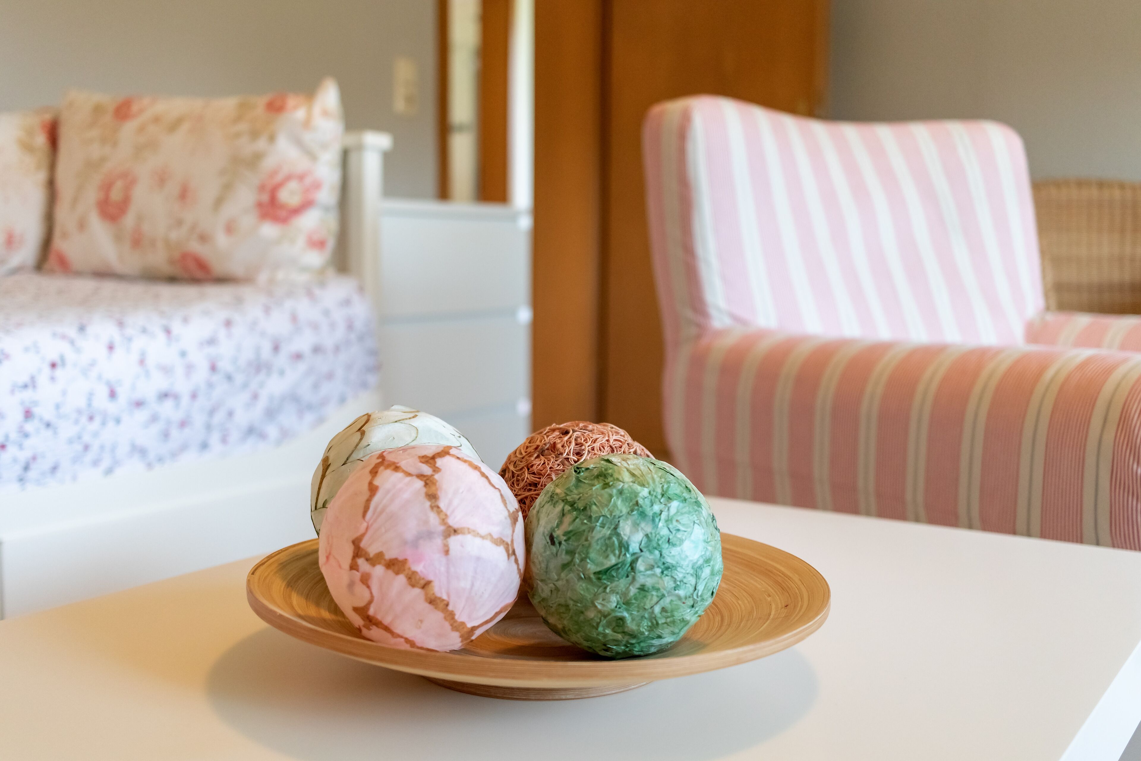 A plate with three ice cream balls on a table in a room with a bed and a striped chair in the background.