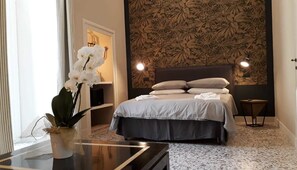 A bedroom with a bed, a bedside table, a vase with flowers, and a wall with a floral pattern. - MammaDada Guest House  (Bari)
