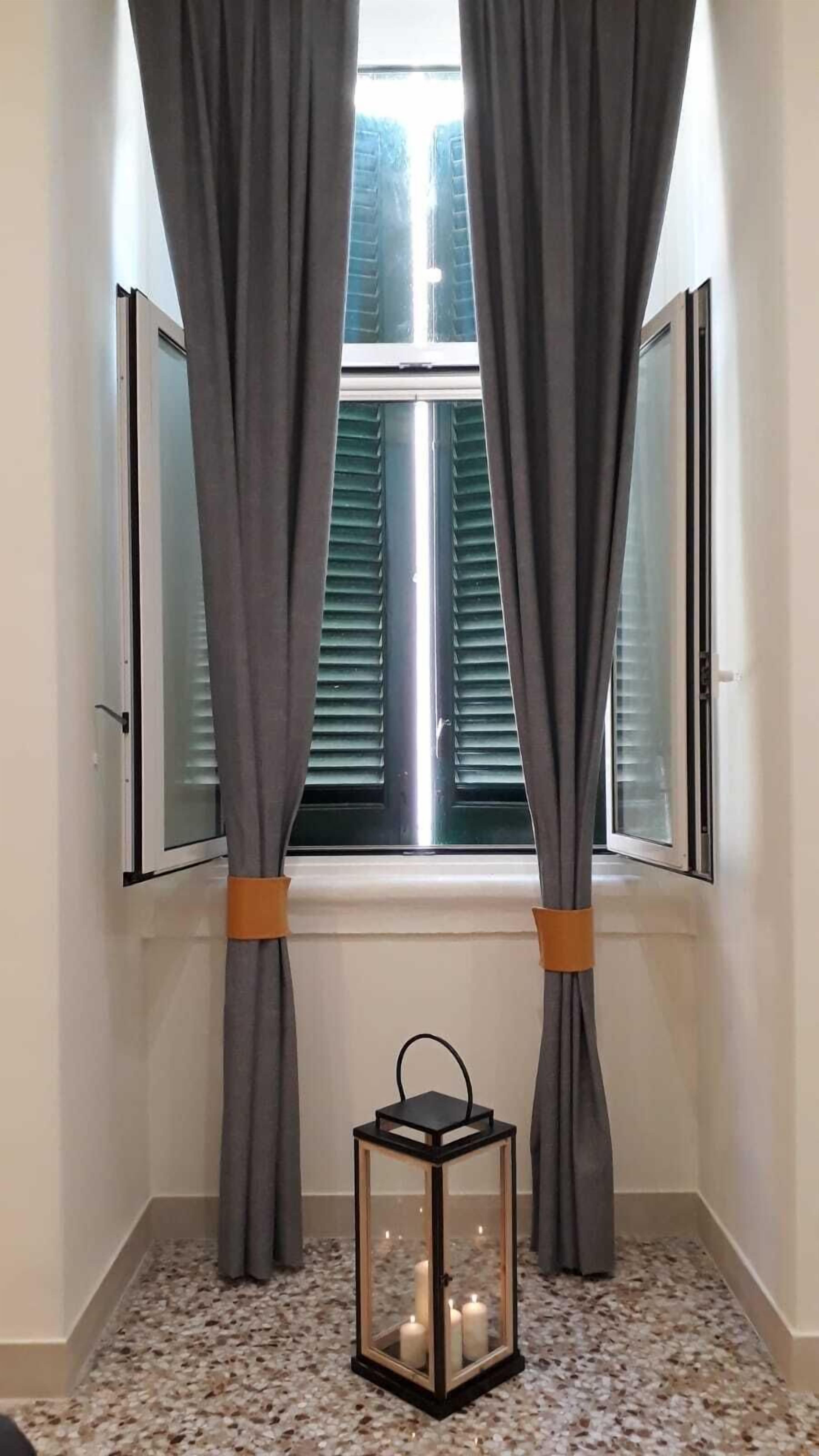 Een kamer met een raam, grijze gordijnen vastgebonden met oranje linten, en een lamp op de vloer.