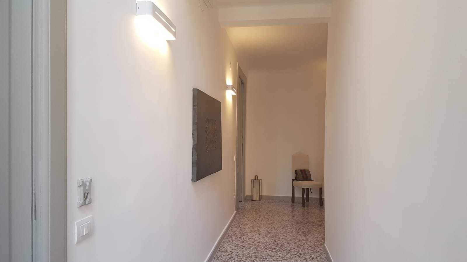 A hallway with a chair and a table, a wall-mounted light fixture, and a door.