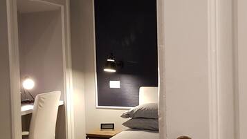 Ein Schlafzimmer mit Bett, Schreibtisch mit Stuhl, Nachttisch und Fenster mit Blick auf den Nachthimmel.