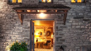 A stone building with a wooden porch, a large potted plant, wicker furniture, and a lantern.