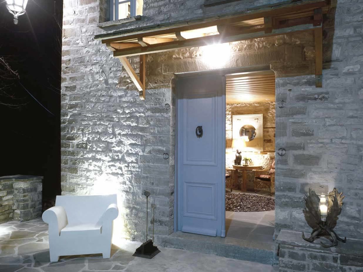 A stone building with a white door, a white chair outside, and a wooden beam structure above the door.