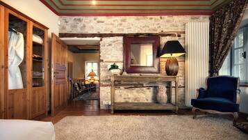 A room with a stone wall, wooden furniture, a blue armchair, and a mirror above a console table.