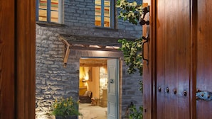 A stone building with a wooden door and a stone pathway leading to a lit interior.