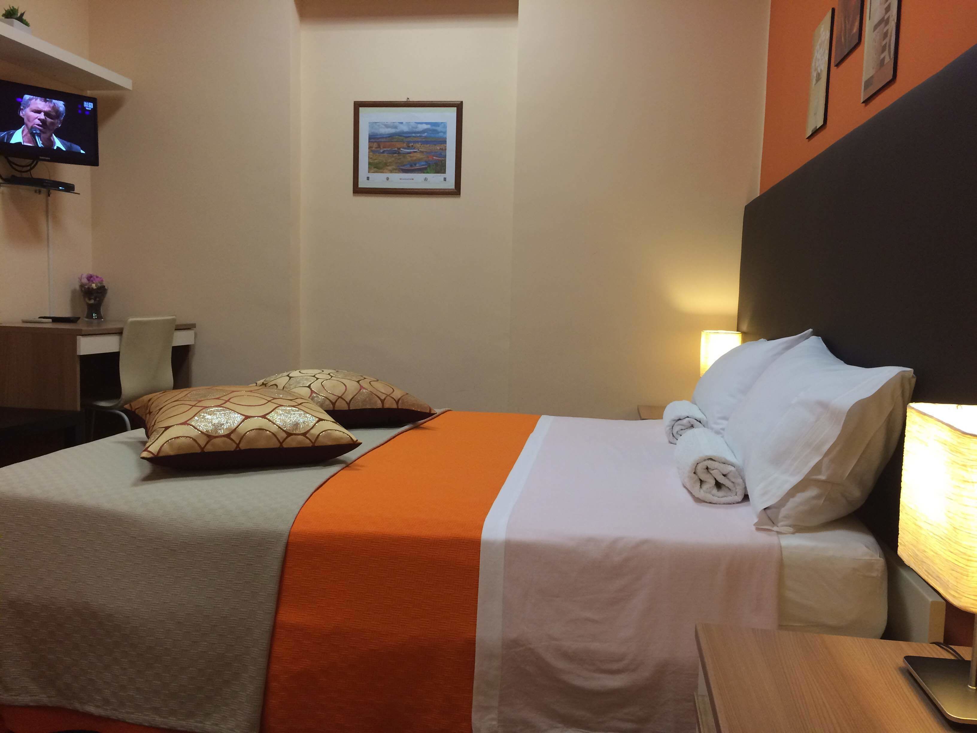 Een hotelkamer met een bed, een bureau, een stoel, een televisie en een lijst aan de muur.