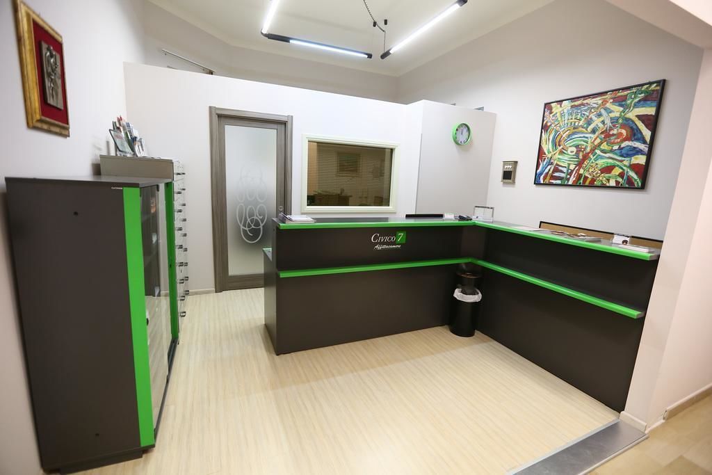 A reception desk with a green accent, a clock, and a colorful abstract painting on the wall.