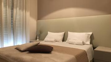 A hotel room with a large bed, two pillows, a nightstand with a lamp, and a window with sheer curtains.