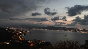 A coastal cityscape at dusk with a view of the sea and distant mountains.