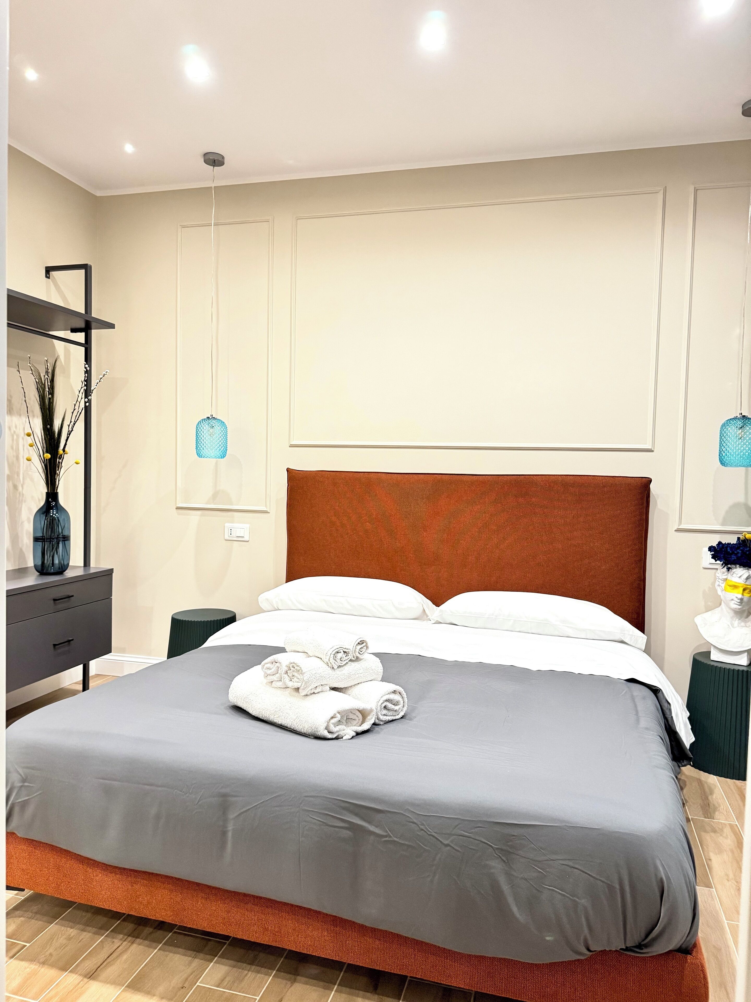 A modern hotel room with a large bed, a nightstand, a dresser, and a mirror.
