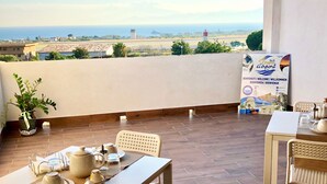 Terraço com mesa posta para chá, um vaso de planta e um letreiro dando as boas-vindas aos visitantes do aeroporto.