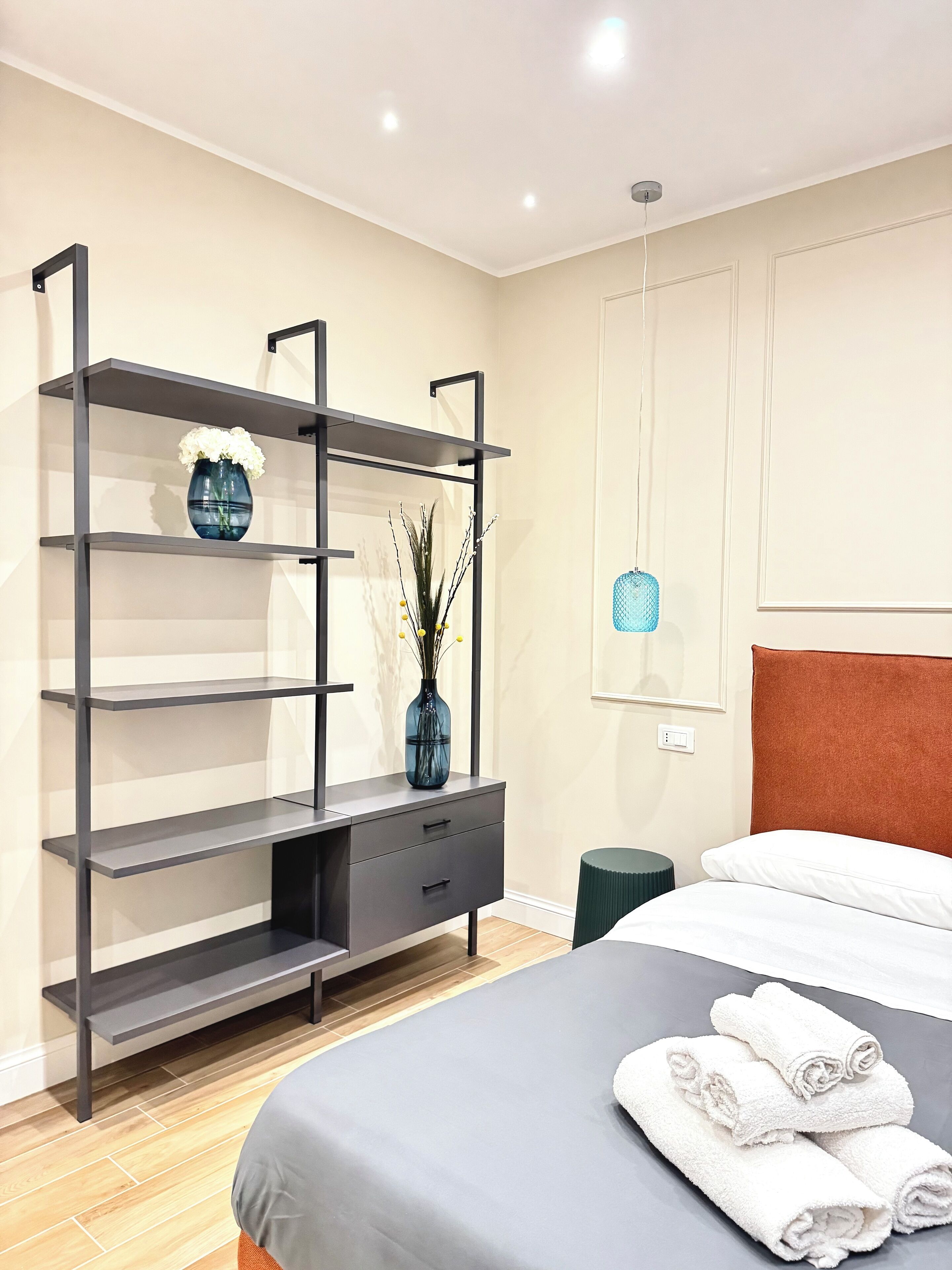 A modern bedroom with a bed, a built-in shelving unit, and a bedside table.