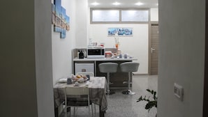 Uma cozinha compacta com micro-ondas, uma pequena mesa de jantar com duas cadeiras e uma janela com painéis de vidro fosco.