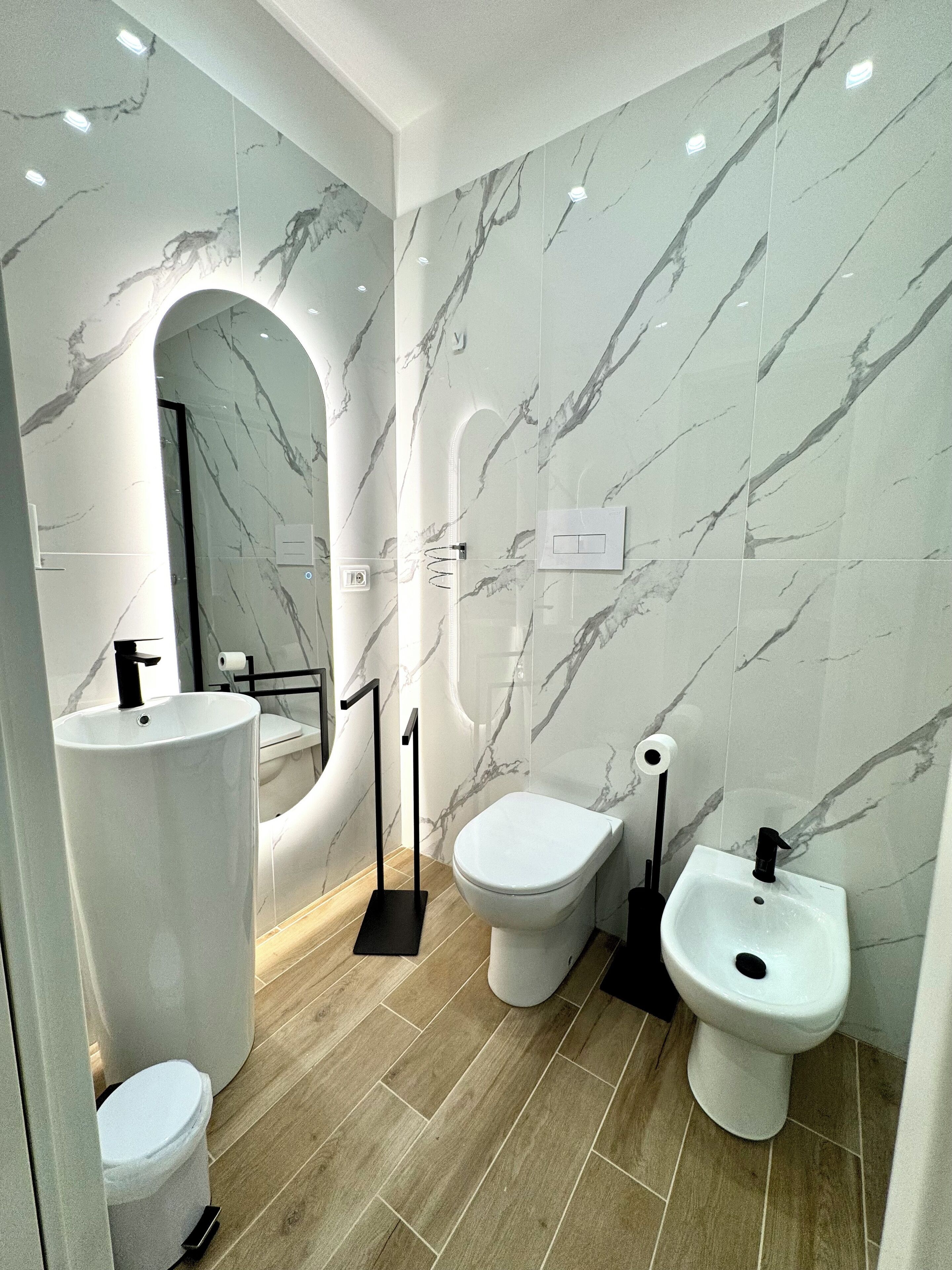 Un baño moderno con paredes de mármol, inodoro, bidé y lavamanos.
