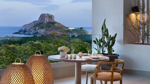 A balcony with a table set for dining, overlooking a coastal landscape with a prominent rock formation.