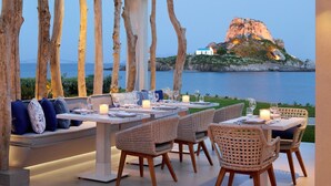 An outdoor dining area with tables and chairs, overlooking a scenic view of the sea and a rocky island.