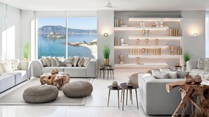 A modern living room with a large window overlooking a coastal view, featuring a grey sofa, round ottomans, and a wooden coffee table.